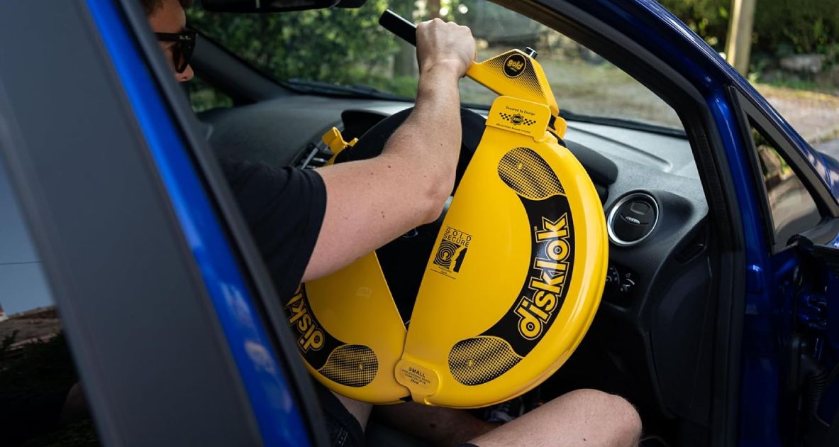 Disklok Steering Wheel Lock product image of someone adding a yellow full wheel cover to their car's steering wheel.