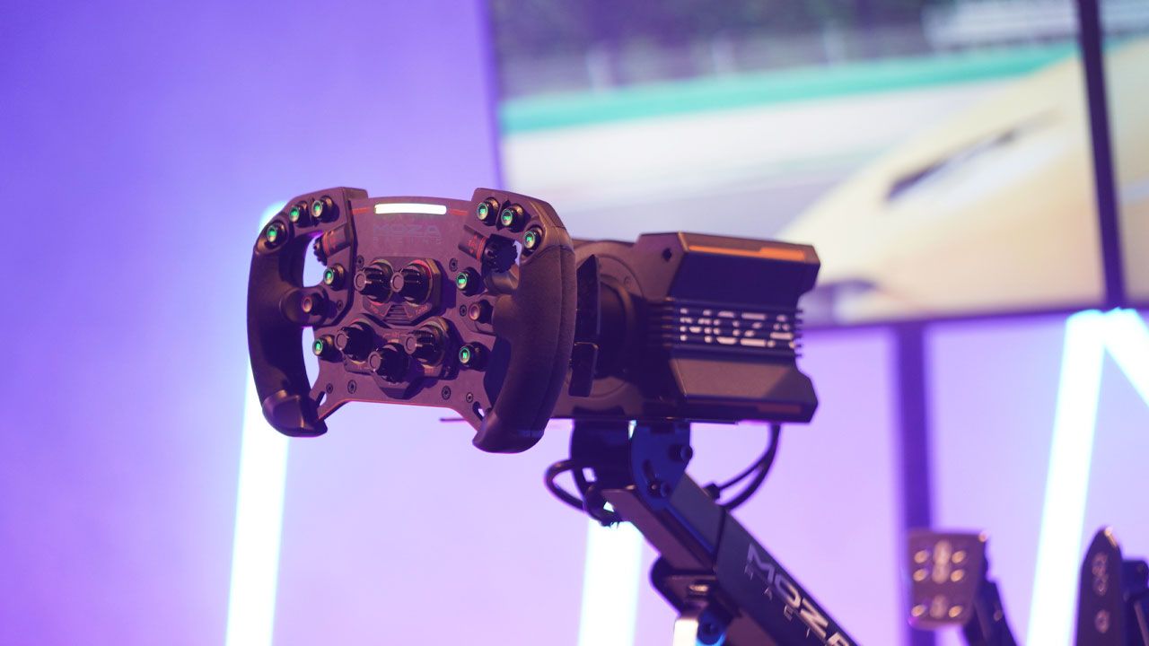 Image of a black Formula-style wheel attached to a black MOZA wheel base in front of a monitor.