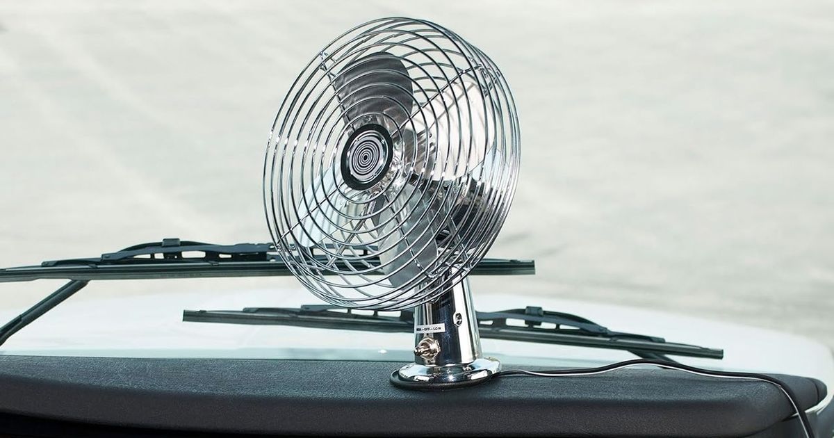 A small, silver, wired fan connected to a car's black dashboard.