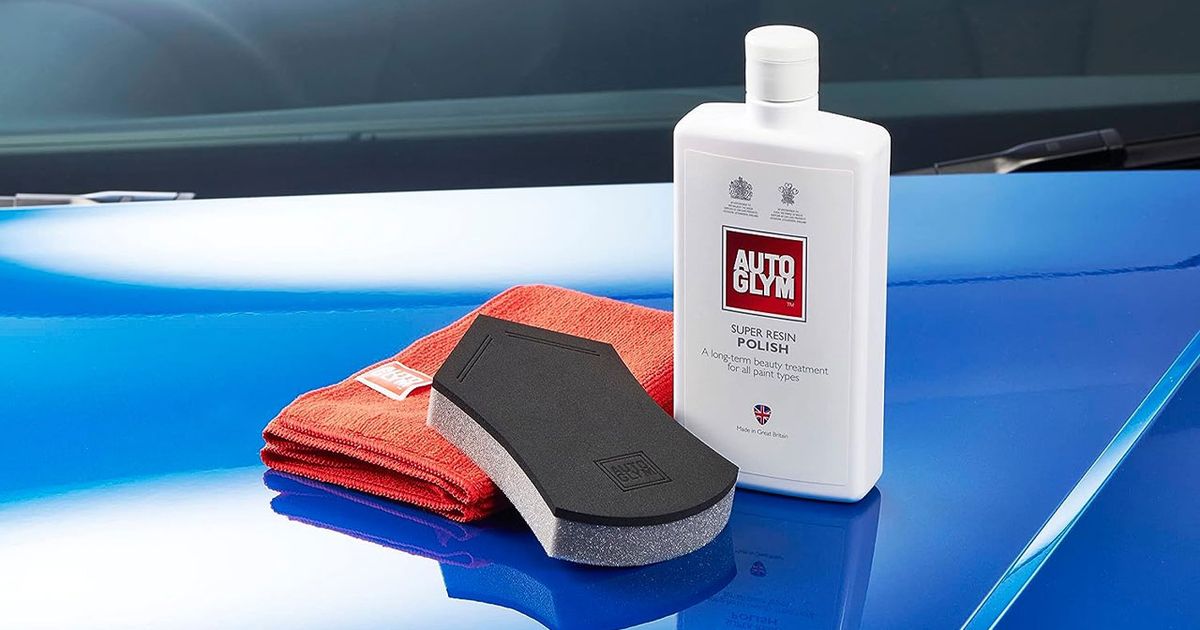 Image of a white bottle of car polish on top of a blue car next to a red cloth and black and grey sponge.