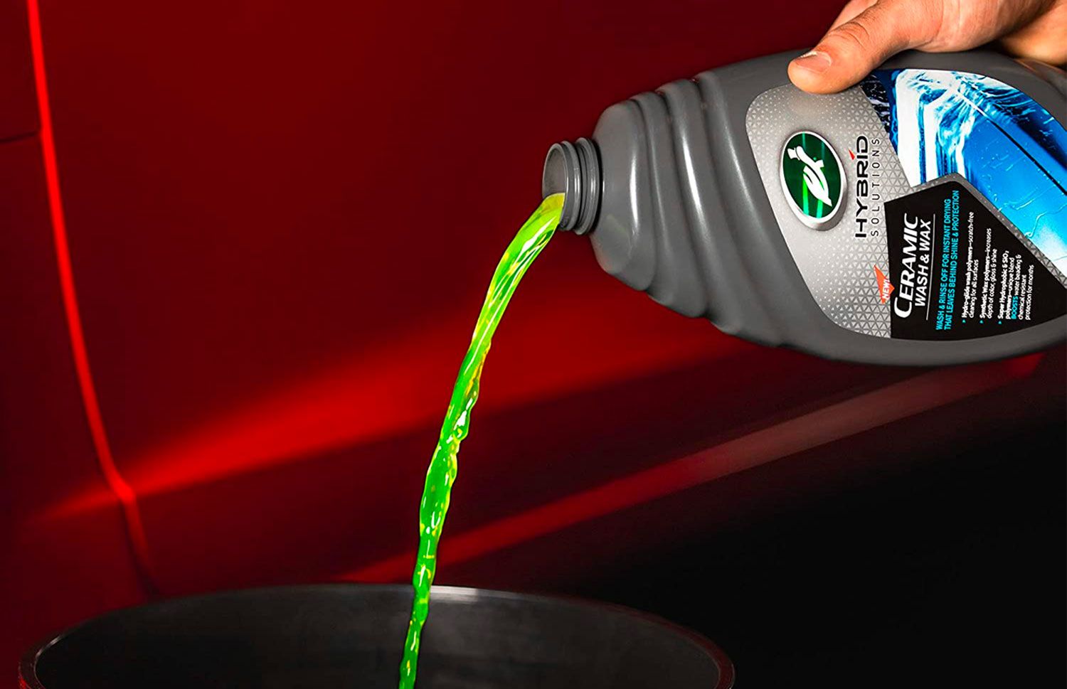 Turtle Wax Hybrid Solutions Ceramic Wash and Wax product image of a grey bottle pouring green car shampoo into a black bucket.