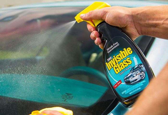 Best car window cleaner Invisible Glass Premium Glass Cleaner product image of a black, blue, and yellow spray bottle being sprayed onto a window.