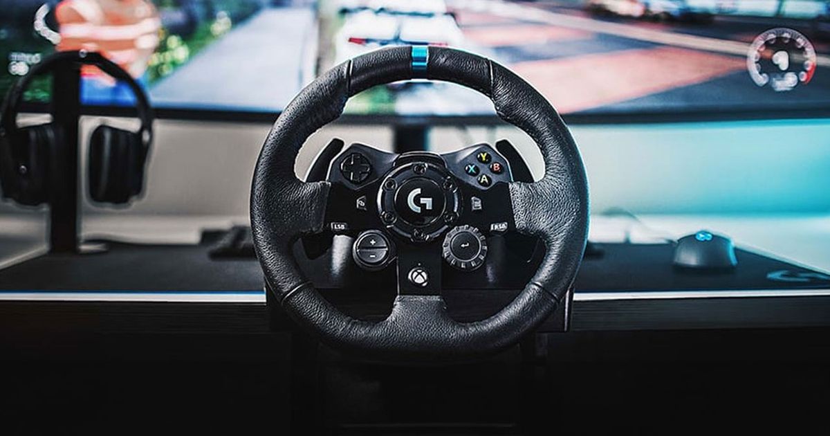 A black racing wheel with a blue centre line at the top in front of an ultrawide monitor.