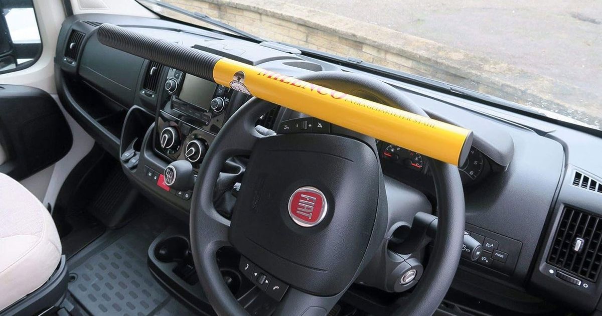 A yellow steering wheel lock attached to a black wheel inside a Fiat.
