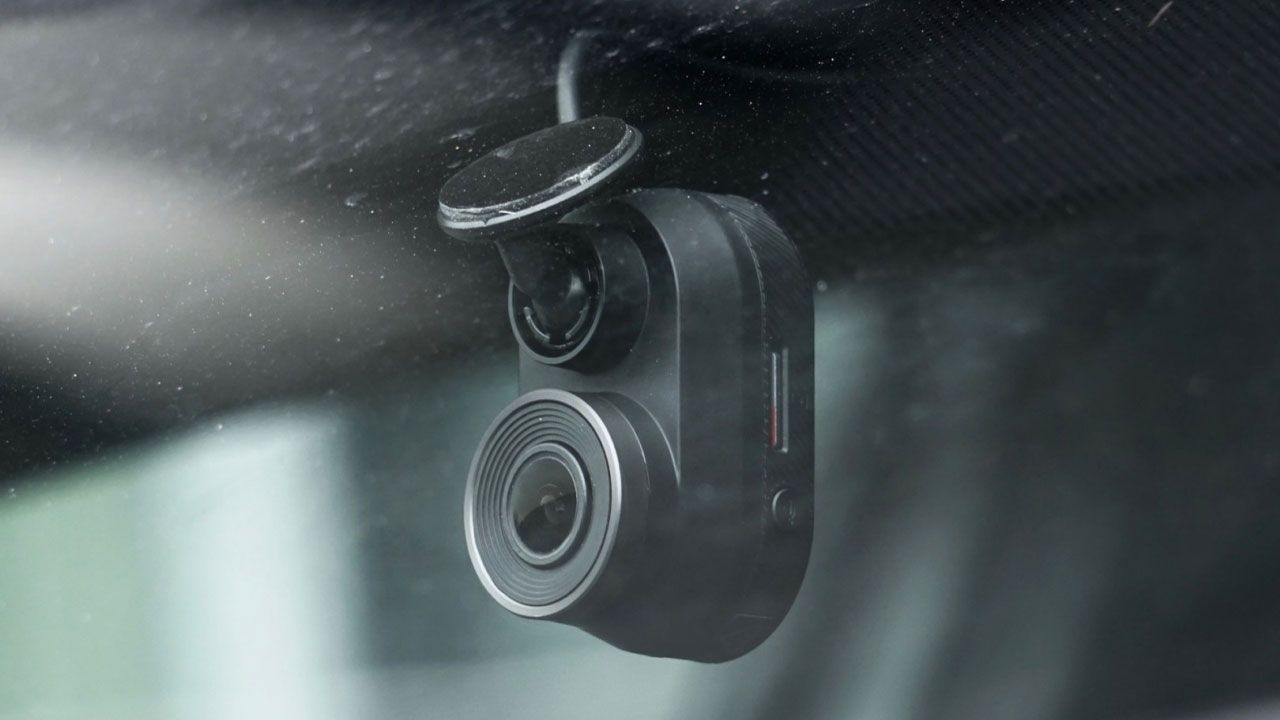 A small black dash camera stuck to a front windscreen of a car.
