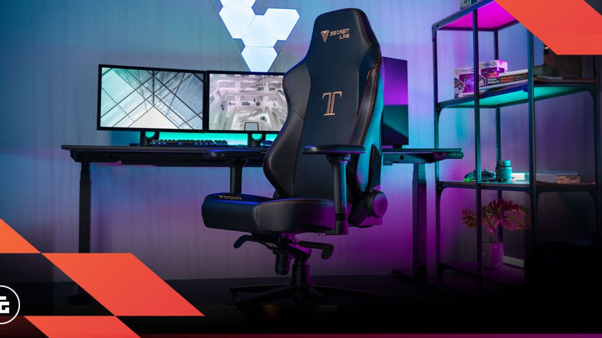 A black gaming chair featuring gold branding in front of a desk and three monitors in a room lit by purple and blue light.