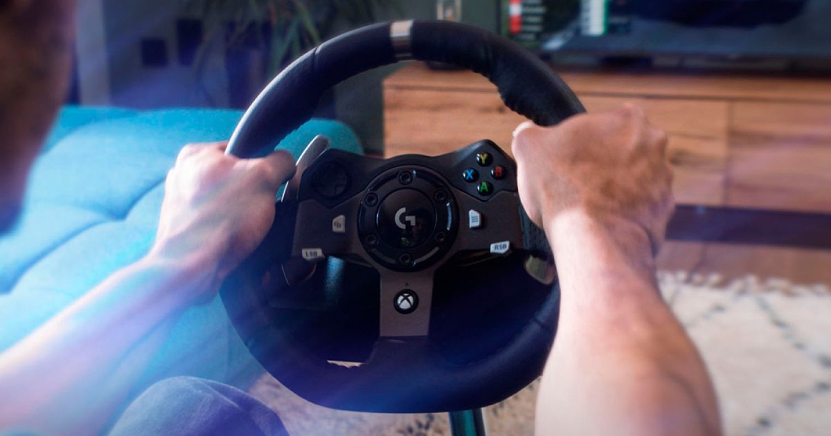 Someone gripping a black racing wheel with multiple buttons on the center console and a grey line at the top of the wheel.