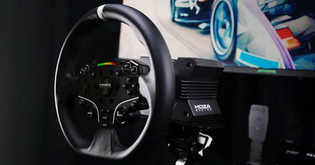 A black sim racing wheel with a white centre line at the top attached to a wheel base in front of a large screen.