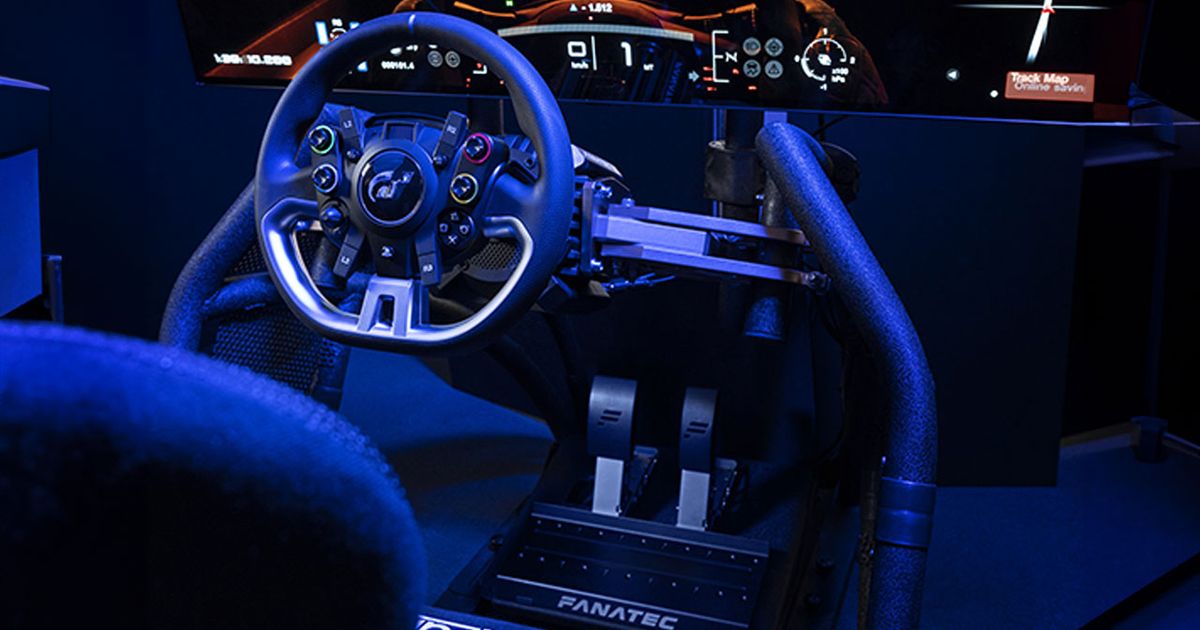 A black racing wheel attached to a rig and TV in front of a racing seat in a darkened room surrounded by blue light.