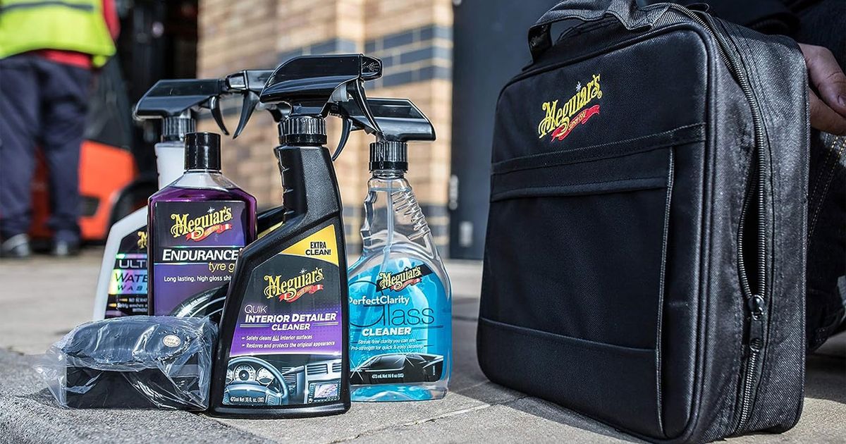 A black bag with yellow and red Meguair's branding on it next to a set of spray bottles containing cleaning solutions.