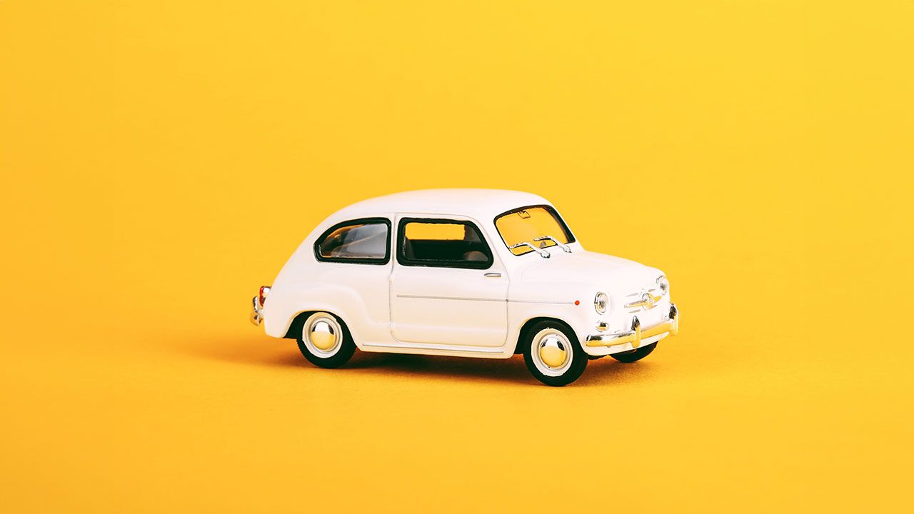 A white Volkswagen Beetle model car in front of an orange background.