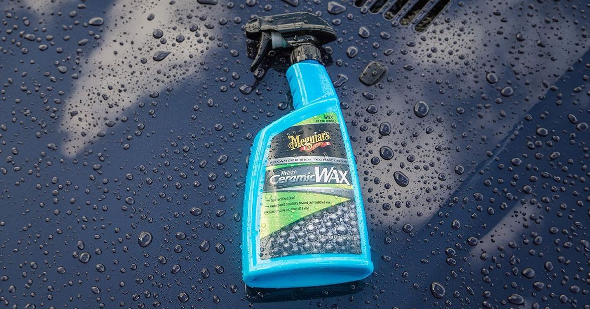 A blue bottle with a black sprayable cap laying on a black car covered in beads of water.