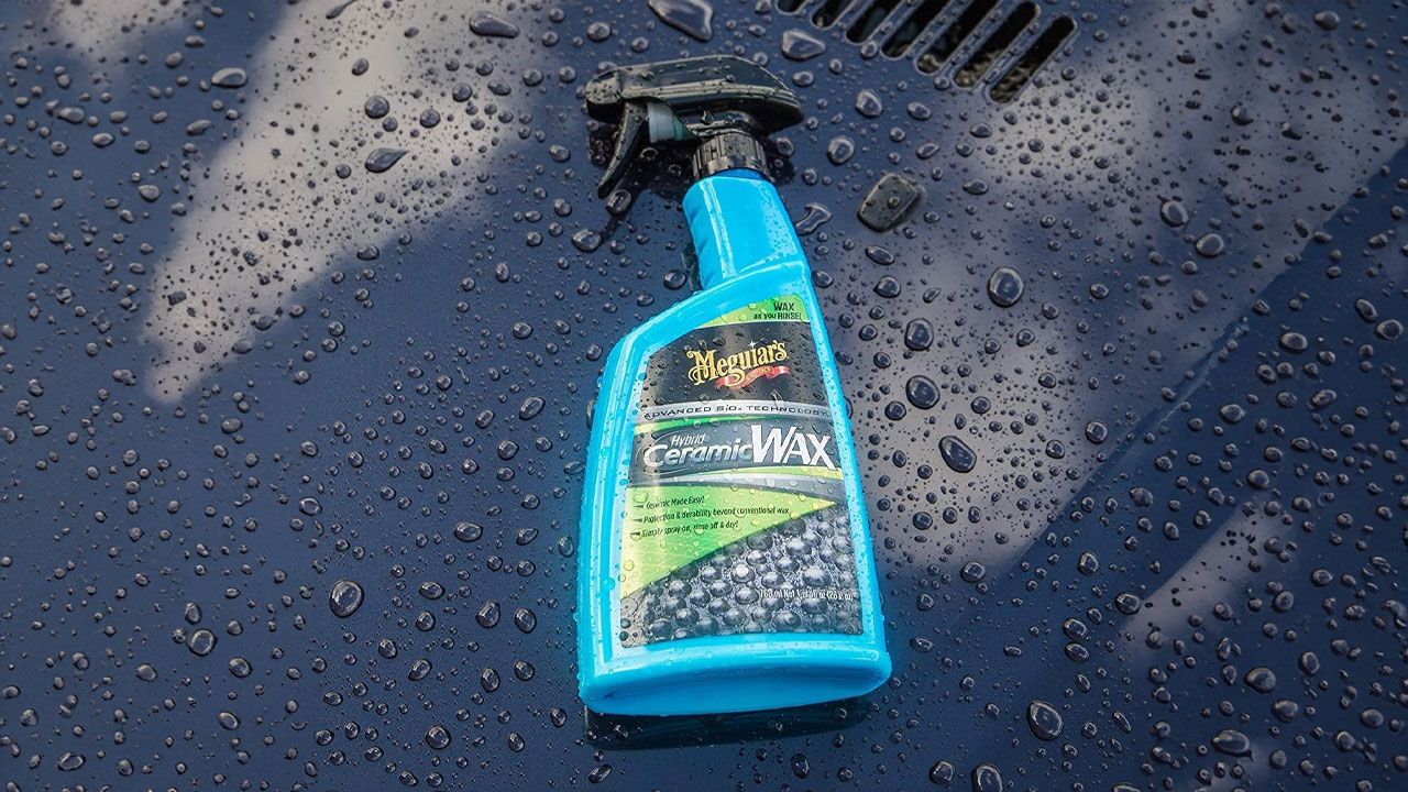 A blue bottle with a black sprayable cap laying on a black car covered in beads of water.