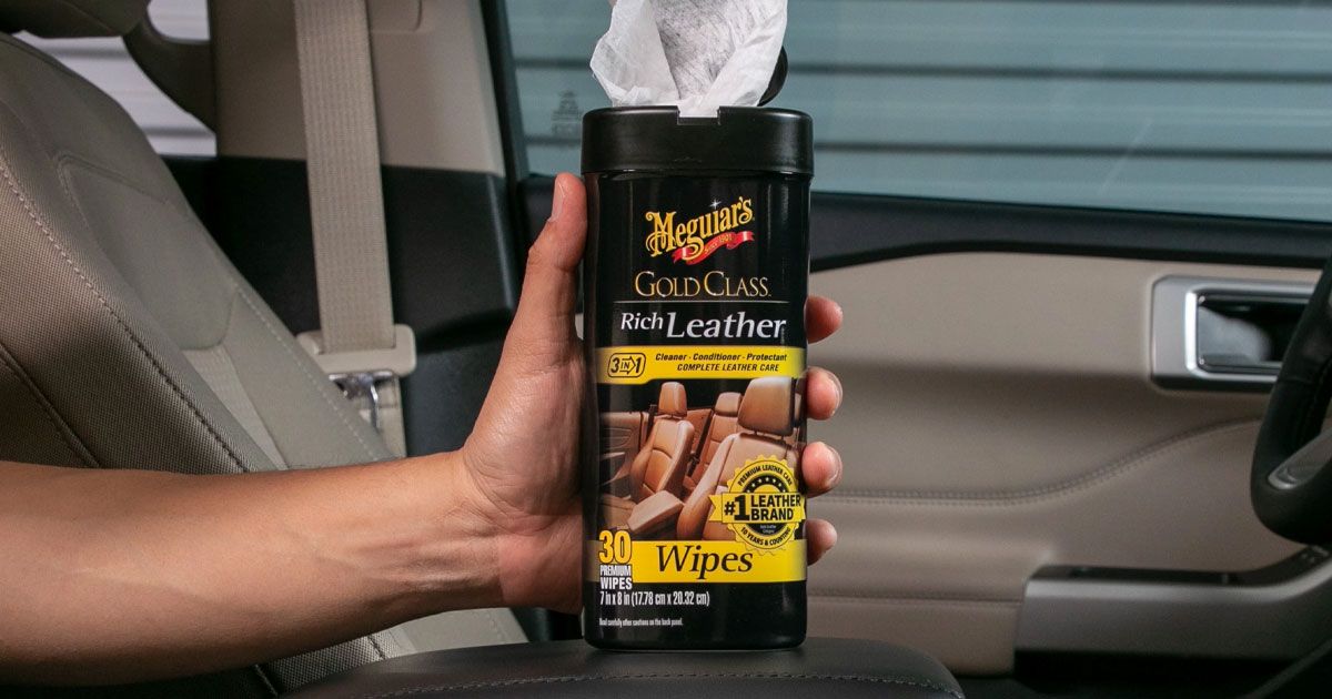 Someone pulling out a white wipe from a black container featuring yellow branding inside a car.