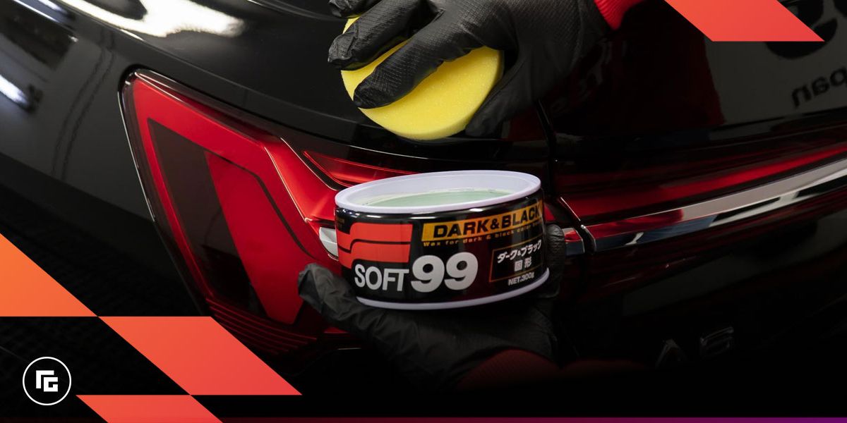 Image of a black tub of car wax being applied by someone in black gloves to a black car with a yellow sponge.